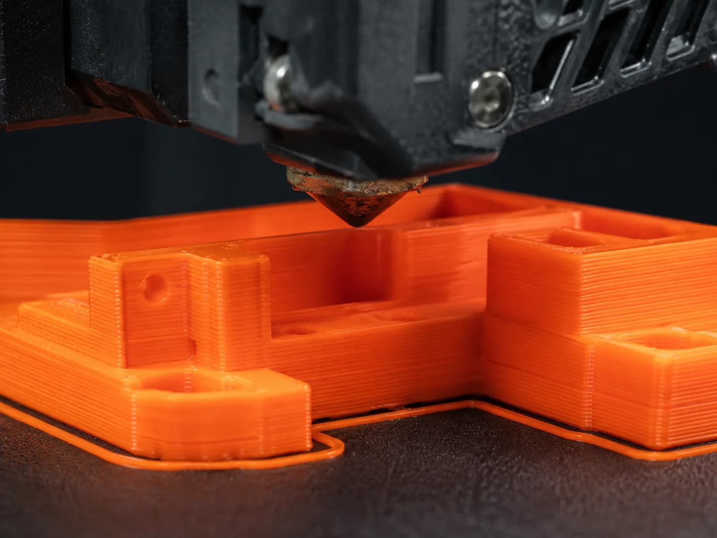 FDM nozzle depositing orange thermoplastic layers